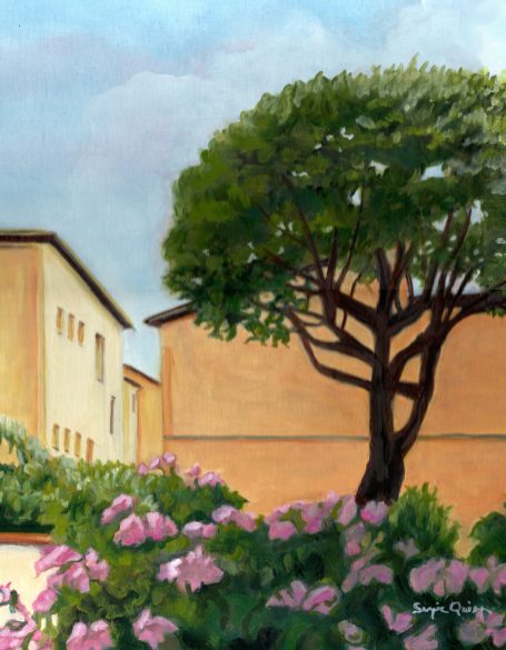 A tree and pink flowers near buildings under a cloudy sky.