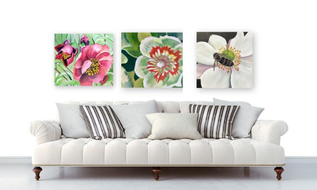 A white couch with striped cushions in front of three floral paintings on a wall.